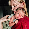 affection, baby, child, closeup, clothing, expression, face, green_cloth, hand, headband, holding, indoor, love, mother, newborn, portrait, red_shirt, skin, tattoo, woman