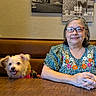 dog, person, woman, portrait, indoors, restaurant, booth, table, wood, glasses, smiling, seated, pet, companion, floral_shirt, vintage_photos, wall, cozy, dinner, photography