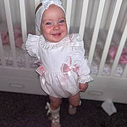 Paula-Cia joined the competition — help win amazing prizes! baby, child, infant, smile, headband, bow, white_dress, crib, furniture, indoors, happy, cute, portrait, standing, footwear, sock, young_child, person, ribbon, floor