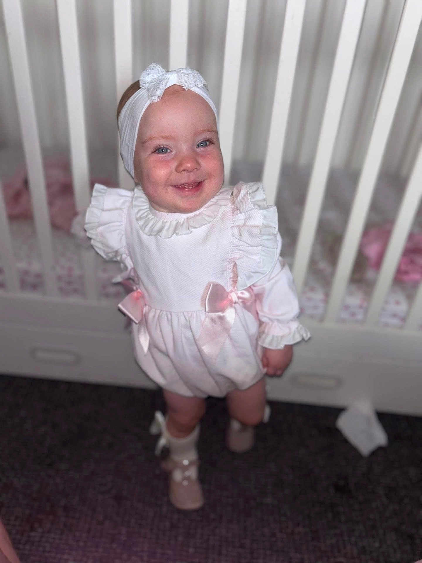 Paula-Cia joined the competition — help win amazing prizes! baby, child, infant, smile, headband, bow, white_dress, crib, furniture, indoors, happy, cute, portrait, standing, footwear, sock, young_child, person, ribbon, floor