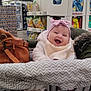 baby, shopping_cart, grocery_store, chips, bag, pink_bow, smiling, clothing, blanket, happy, indoor, person, headwear, retail, aisle, food, seat, jacket, footwear, warm_clothing