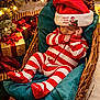 baby, sleeping, christmas, santa_hat, striped_pajamas, wicker_basket, cushion, holiday_lights, gift_box, red_ribbon, festive, decorations, cozy, infant, holiday_season, christmas_tree, indoors, soft_lighting, cute, holiday_spirit