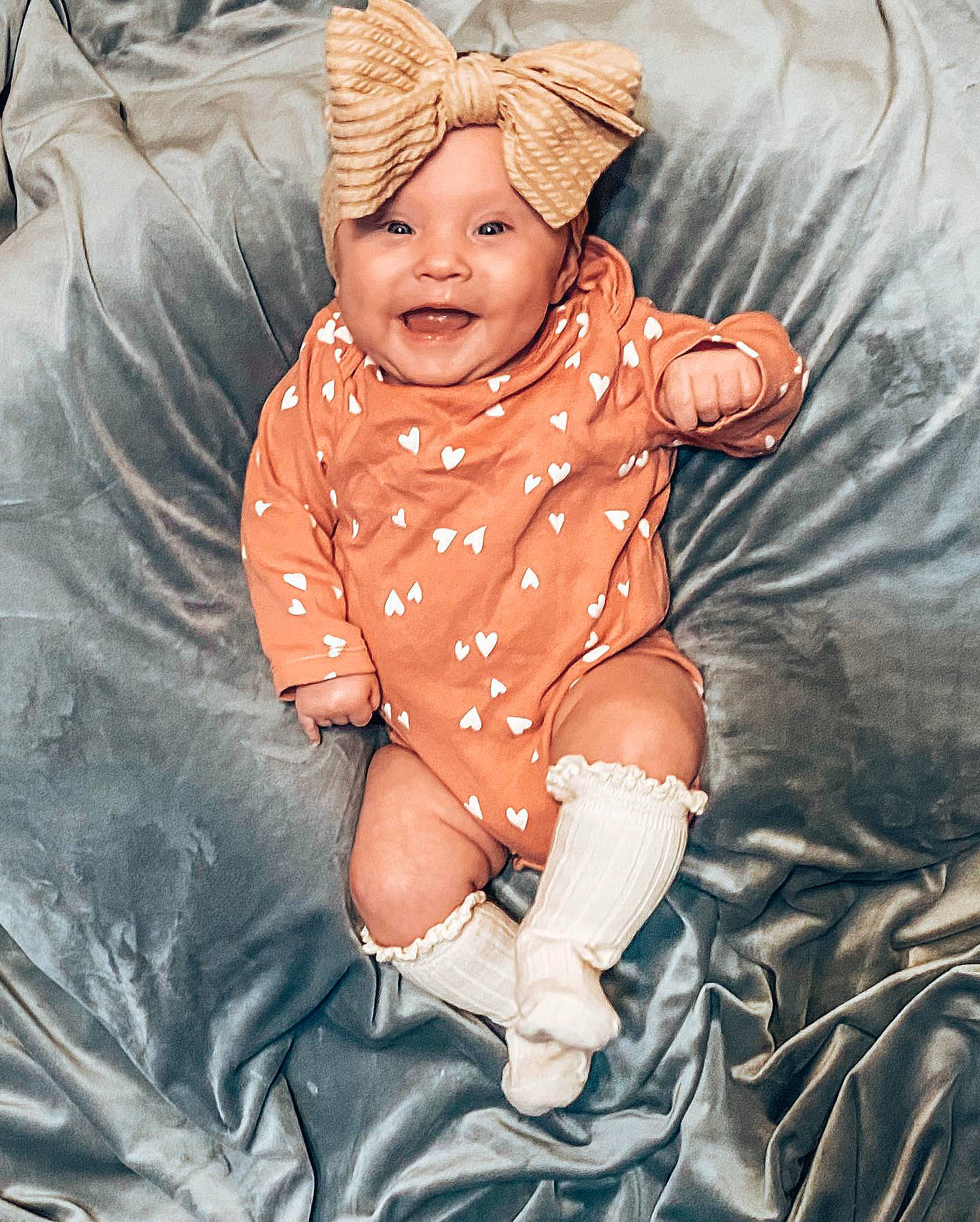 Annabella is registered to the contest to win money with this photo: arm, baby, baby_toddler_clothing, cap, child, comfort, eye, happy, hat, head, headgear, headwear, human_body, mouth, orange, pattern, person, pink, sleeve, smile