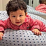 baby, child, pajamas, red_stripes, star_pattern, cushion, mirror, indoor, smile, curly_hair, face, hand, reflection, cute, infant, lying_down, soft_texture, cozy, bright_eyes, portrait
