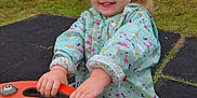 Orlagh joined the competition — help win amazing prizes! child, toddler, pigtails, rain_suit, playground, orange_handle, grass, outdoor, smiling, happy, play_equipment, cloudy_sky, park, cute, young_child, casual_clothing, fun, daytime, nature, play