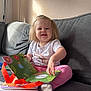 Orlagh is registered to the contest to win money with this photo: toddler, child, book, reading, couch, sofa, indoor, blonde_hair, white_shirt, pink_pants, sock, smiling, happy, natural_light, window_light, home, cozy, person, furniture, playtime