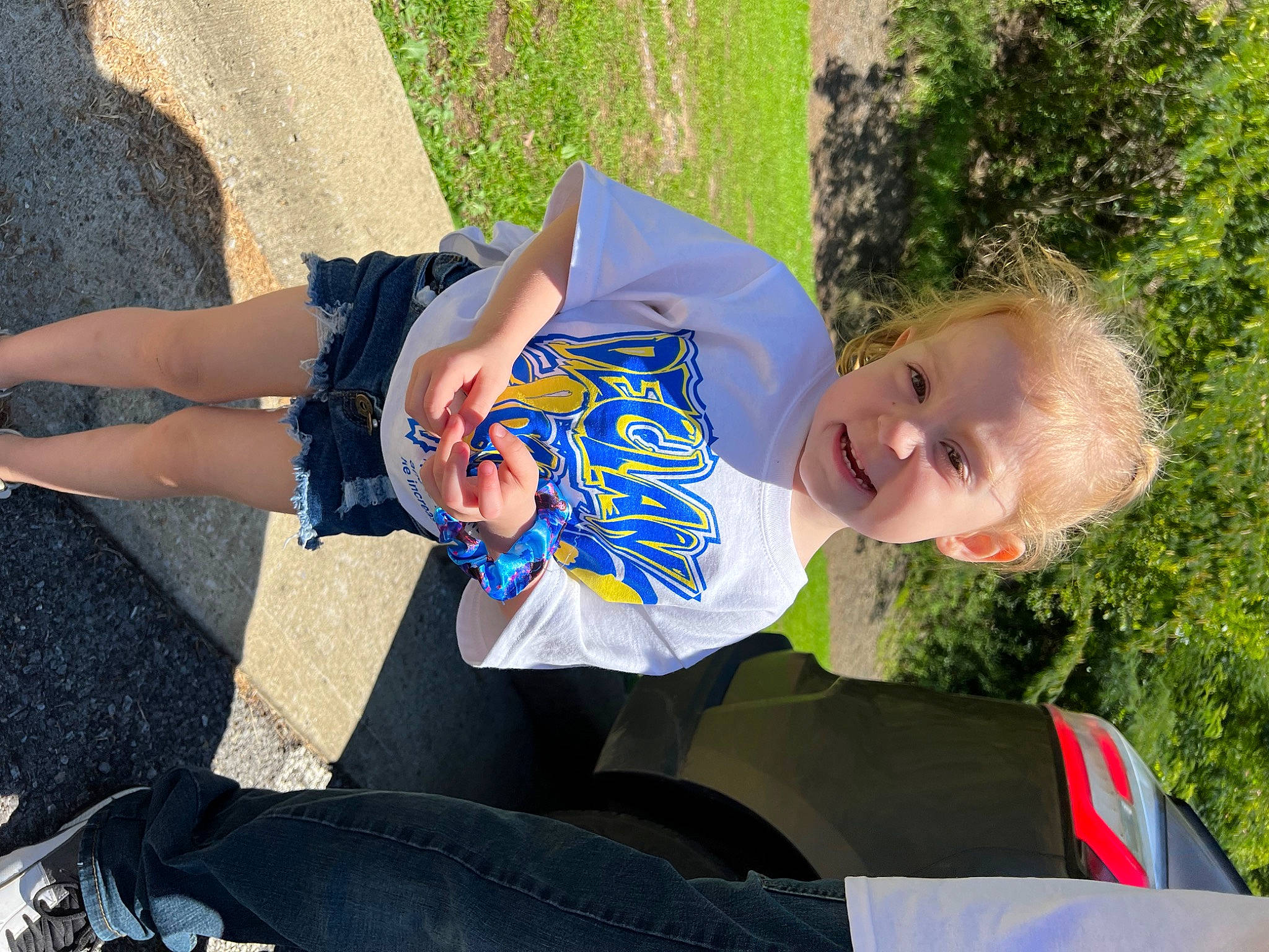 Nevaeh is registered to the contest to win money with this photo: child, denim, electric_blue, eyewear, fun, grass, happy, human_leg, knee, leisure, person, recreation, shadow, sitting, smile, t_shirt, thigh, toddler, tree, vacation