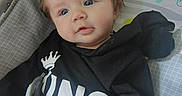 Bellamy is registered to the contest to win money with this photo: baby, infant, blue_eyes, black_shirt, king_text, tousled_hair, baby_mat, rainbow, cartoon_characters, colorful_background, cute, lying_down, indoors, portrait, smiling, child, person, soft_lighting, cozy, closeup