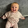 Mabel is registered to the contest to win money with this photo: baby, child, smiling, blue_eyes, pink_clothing, floral_pattern, knitted_blanket, sitting, cute, portrait, indoor, happy, infant, cozy, soft_texture, young_child, face, head, hands, legs