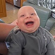 Lucas is registered to the contest to win money with this photo: baby, child, smiling, happy, indoor, living_room, person, clothing, sleeve, zipper, couch, furniture, kitchen, cabinet, floor, hand, skin, head, face, expression