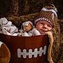 baby, infant, bucket, football, football_hat, pajamas, plush_blanket, soft_texture, cute, cozy, child, portrait, knitted_hat, sports_theme, brown, sleepy, resting, toy, indoor, cute_outfit