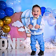 William is registered to the contest to win money with this photo: toddler, boy, birthday, celebration, balloons, blue_suit, bow_tie, number_one, smiling, face, standing, party, decorations, clouds, floor_reflection, festive, happy, indoor, child, portrait