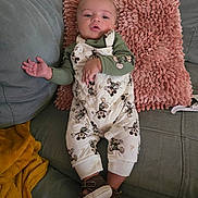 Onofre is registered to the contest to win money with this photo: baby, infant, couch, pillow, clothing, mickey_mouse, footwear, shoe, green_shirt, pink_pillow, gray_couch, person, cute, indoors, child, sitting, relaxed, expression, hand, comfortable