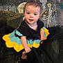 baby, background_art, black_fabric, child, colorful_clothing, costume, crocheted_dress, cute, face, fantasy, ghost_figure, indoor, planets, portrait, seated, smiling, space_theme, stars, whimsical, young_child