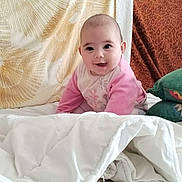 Kaïlyne a rejoint le concours — aidez-le/la à gagner de superbes lots ! baby, child, smiling, pink_clothing, white_blanket, cushion, bed, indoor, cute, portrait, face, young, infant, happy, soft, cozy, sitting, person, blanket, home