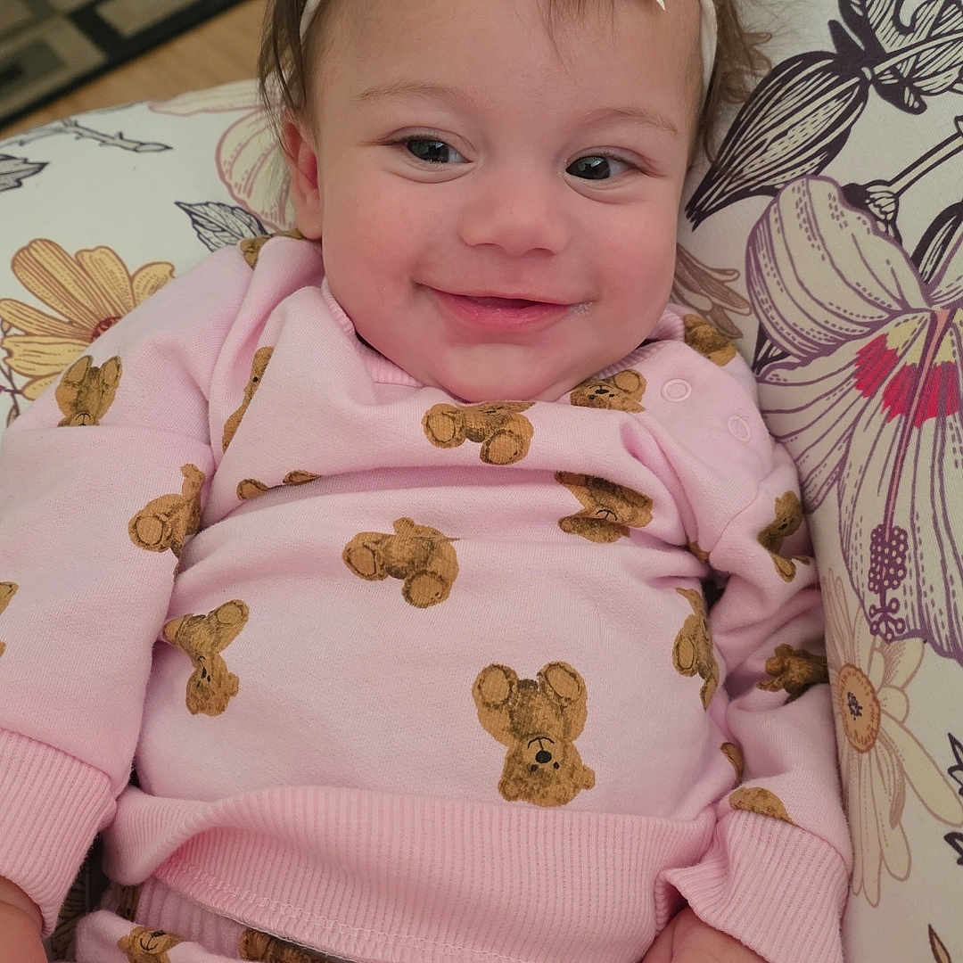 Kaliana is registered to the contest to win money with this photo: baby, bow, child, comfort, cushion, cute, face, floral_pattern, hand, happy, headband, indoors, infant, pink_clothing, portrait, relaxing, smile, soft_toys, teddy_bear_pattern, young_child