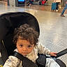 baby, child, stroller, curly_hair, indoor, public_space, people, floor, luggage, seated, walking, casual_clothing, shopping_bag, stairs, advertisement, helmet, person, waiting, urban, travel