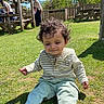child, toddler, grass, outdoor, sunny, barefoot, curly_hair, smile, casual_clothing, picnic_shelter, bench, tree, blue_sky, people, park, daylight, relaxation, nature, playful, happy