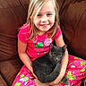 child, girl, cat, pet, pajamas, pink_clothing, gray_cat, couch, indoor, smiling, sitting, holding, furry_pet, cute, cozy, happy, young, animal, home, relaxed