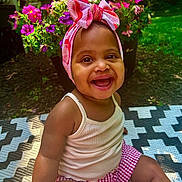Natalia is registered to the contest to win money with this photo: baby, child, smiling, headband, outdoor, flower, greenery, patterned_mat, happy, cute, summer, sunlight, skin, tank_top, shorts, pink, red, nature, sitting, portrait