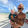 beach, baby, man, tattoos, sunglasses, ocean, sand, clouds, sky, water, child, holding, summer, sunny, shore, people, casual, outdoor, vacation, family