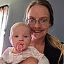 baby, woman, glasses, pacifier, smile, indoor, curtain, person, child, holding, face, portrait, long_hair, light, clothing, hand, room, casual, young_child, happy