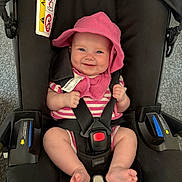 Vaughn is registered to the contest to win money with this photo: baby, car_seat, smile, pink_hat, pink_striped_clothing, infant, seat_belt, happy, child, foot, hand, indoor, fabric, black_car_seat, headwear, person, cute, safety_harness, cheeks, straps