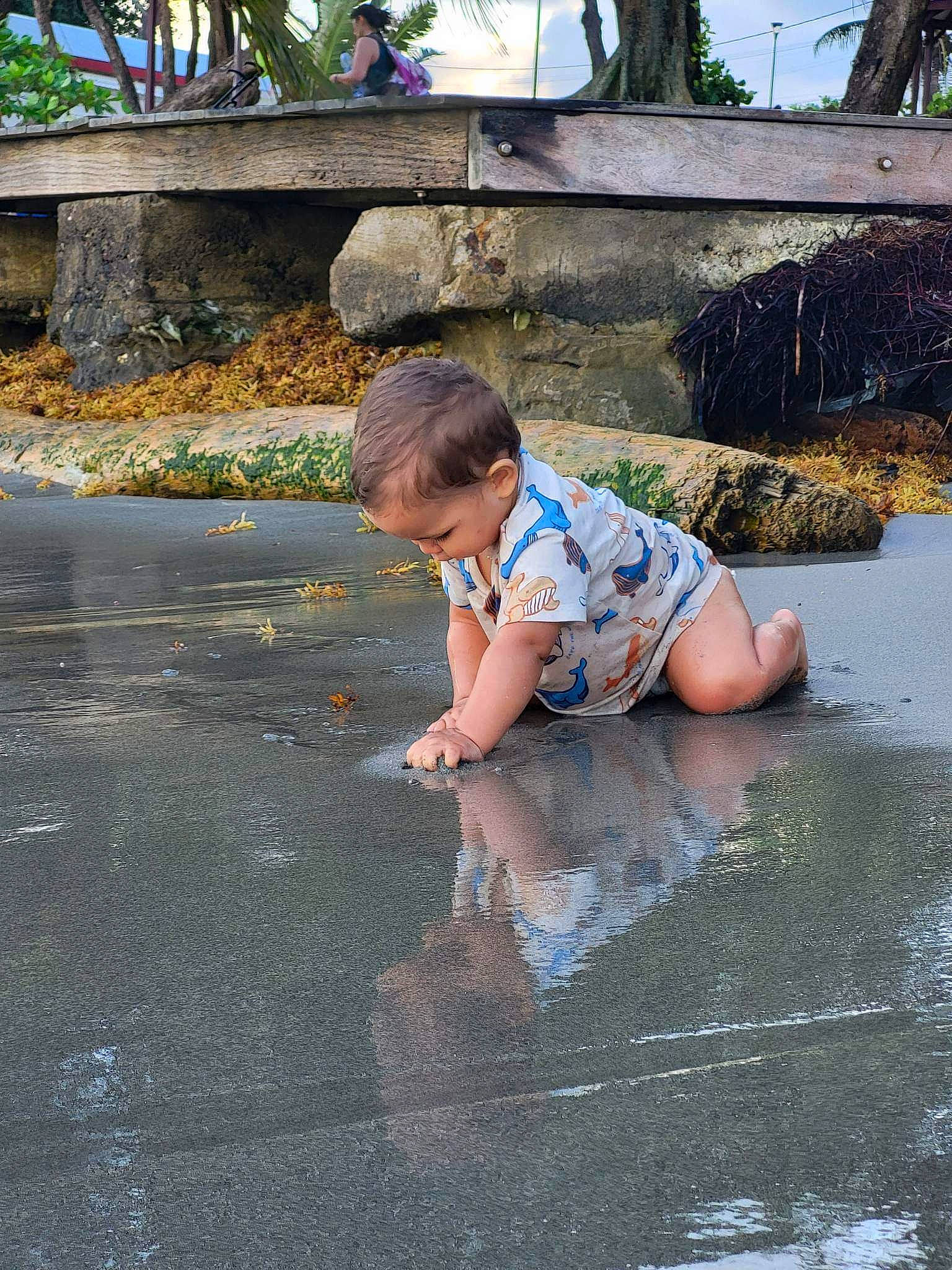 Zackary a rejoint le concours — aidez-le/la à gagner de superbes lots ! asphalt, barefoot, concrete, flooring, fun, grass, leisure, person, plant, puddle, recreation, road, road_surface, sidewalk, sitting, soil, t_shirt, toddler, tree, water