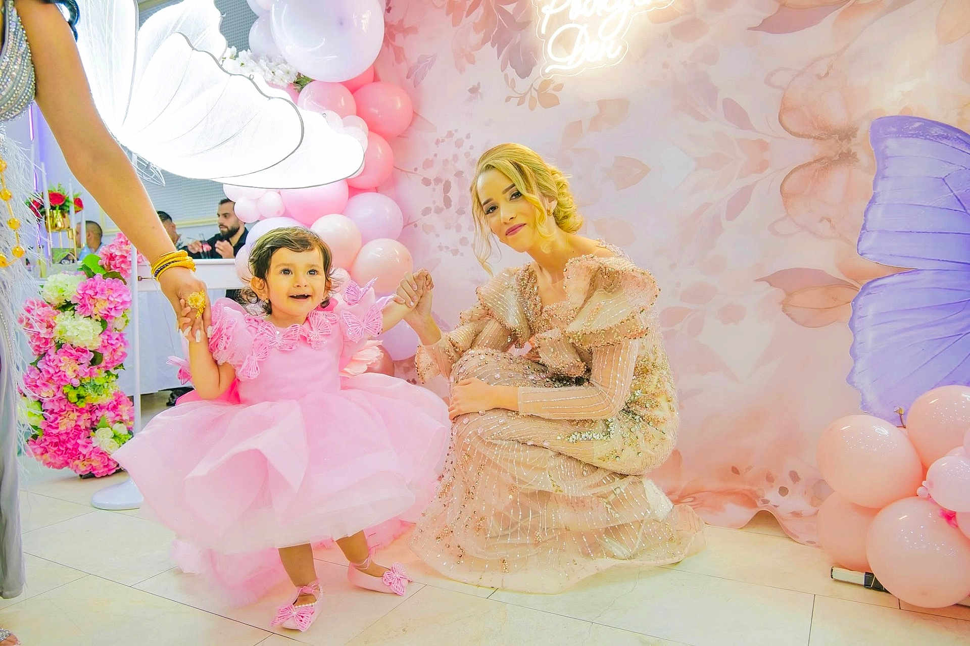 Veska is registered to the contest to win money with this photo: child, toddler, pink_dress, balloons, flowers, woman, party, celebration, indoor, decorations, smiling, holding_hands, dress, butterfly, floor, happy, event, person, curly_hair, light
