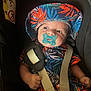 baby, car_seat, child, clothing, colorful, cute, face, hands, hat, indoors, infant, looking, pacifier, person, portrait, safety_harness, seatbelt, sitting, tropical_print, young
