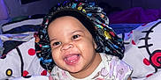 London joined the competition — help win amazing prizes! baby, bed, blanket, bonnet, child, colorful, cozy, cute, face, furniture, happy, home, indoors, onesie, patterned_clothing, person, portrait, sitting, smiling, television