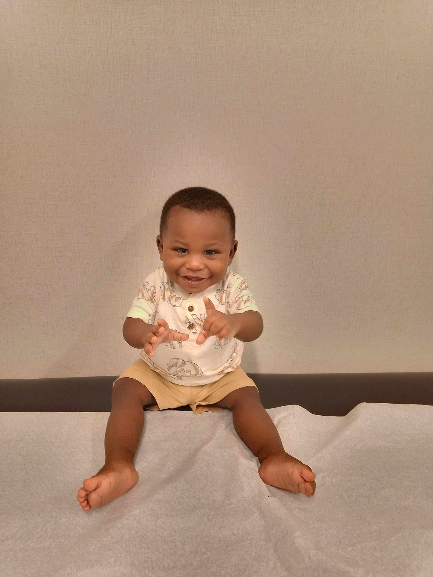 Ke'Vontae is registered to the contest to win money with this photo: toddler, child, smiling, sitting, shorts, shirt, barefoot, indoor, medical_table, paper_sheet, playful, happy, person, young_child, portrait, baby, furniture, wall, cute, hands