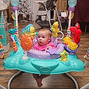 Arianna joined the competition — help win amazing prizes! baby, child, indoor, activity_jumper, toys, sea_creatures, floor, wood_floor, high_chair, christmas_tree, curious, pink_clothing, playful, colorful, furniture, home, infant, seat, purple, yellow