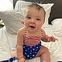 baby, infant, child, smiling, sitting, bed, pillow, blanket, indoors, clothing, swimsuit, stars, stripes, happy, cute, skin, face, hair, hand, blue