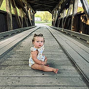 Laelynn is registered to the contest to win money with this photo: toddler, child, covered_bridge, wooden_floor, outdoor, sitting, curly_hair, pigtails, summer_clothes, innocent, portrait, nature, daylight, rustic, wood, planks, expression, looking_up, alone, quiet