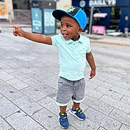 Paul participe au concours pour gagner de l'argent avec cette photo : child, toddler, boy, cap, blue_cap, polo_shirt, mint_shirt, shorts, gray_shorts, sneakers, blue_sneakers, sidewalk, street, urban, pointing, happy, smiling, outdoor, daylight, person