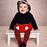 Leïo participe au concours pour gagner de l'argent avec cette photo : baby, background, bench, black, carpet, child, clothing, costume, cute, ears, happy, hoodie, indoor, person, portrait, red, sitting, smile, striped_tights, toddler