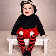 Leïo a rejoint le concours — aidez-le/la à gagner de superbes lots ! baby, bench, black, carpet, child, clothing, costume, cute, happy, hoodie, indoor, mickey_mouse, person, portrait, red, sitting, smiling, striped_tights, studio, young_child