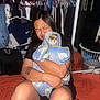 Chubby is registered to the contest to win money with this photo: person, cat, towel, hugging, indoor, clothes, hanger, laundry_basket, bed, blanket, tattoo, bracelet, ring, long_hair, black_shirt, orange_blanket, closet, mirror, furniture, home