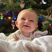 Evelyn joined the competition — help win amazing prizes! baby, smile, blanket, christmas_tree, ornaments, holiday, festive, happy, infant, cozy, cute, indoors, decorations, seasonal, child, portrait, warm, soft, celebration, tree