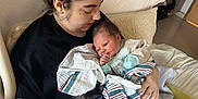 Dean is registered to the contest to win money with this photo: newborn, baby, woman, hospital_bed, hospital_room, blanket, medical_equipment, pacifier, bracelet, curly_hair, holding, tender, bed, cabinet, blanket_tassels, phone, person, face, indoor, family