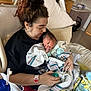 newborn, baby, woman, hospital_bed, hospital_room, blanket, medical_equipment, pacifier, bracelet, curly_hair, holding, tender, bed, cabinet, blanket_tassels, phone, person, face, indoor, family