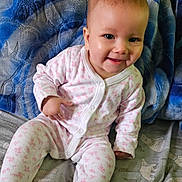 Elizabeth is registered to the contest to win money with this photo: baby, child, smiling, onesie, blanket, bed, blue, pink, pattern, animal_print, happy, cute, indoors, person, portrait, seated, soft_texture, cozy, young, infant