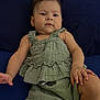 baby, infant, child, green_clothing, cushion, navy_blue, portrait, relaxing, indoor, cute, smiling, person, furniture, skin, hand, foot, earrings, shorts, top, bracelet
