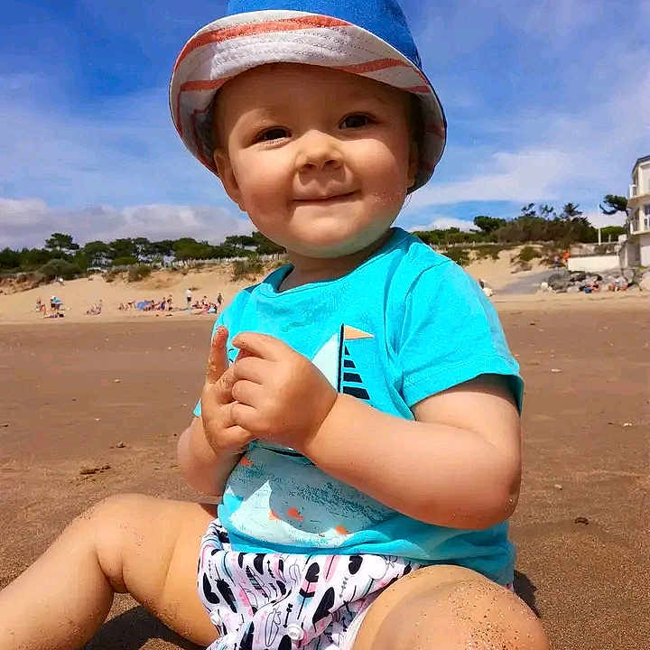 Lilouan participe au concours pour gagner de l'argent avec cette photo : barefoot, beach, blue_sky, casual_clothing, child, happy, hat, nature, outdoor, playful, portrait, sand, sand_on_skin, sitting, smile, summer, sunlight, sunny_day, toddler, vacation