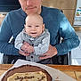 baby, man, child, birthday_cake, cake, kitchen, wooden_cabinet, microwave, oven, table, happy, smiling, portrait, celebration, family, indoor, person, food, clothing, male