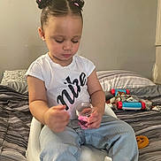 Kaomi joined the competition — help win amazing prizes! child, toddler, sitting, bed, booster_seat, toy, jar, pink, hair_buns, hair_ties, clothing, jeans, tshirt, indoor, blanket, pillow, furniture, person, focus, play