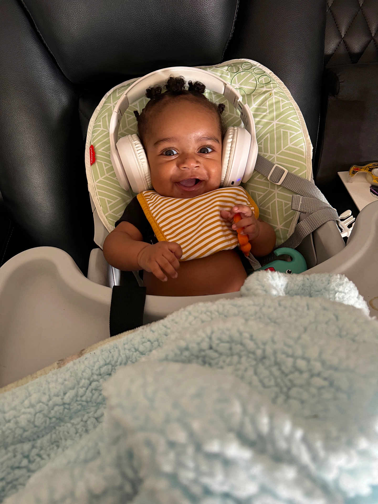 Nash Griffin is registered to the contest to win money with this photo: baby, headphones, high_chair, bib, toy, blanket, smiling, happy, indoor, child, hair_buns, black_leather, seat_belt, close_up, infant, cute, playful, person, baby_accessories, comfort