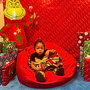 Catilayah is registered to the contest to win money with this photo: toddler, child, bean_bag, red, christmas, holiday, presents, wrapped_gifts, inflatable_grinch, candy_cane, festive_dress, blue_carpet, indoor, smiling_face, decorations, background, celebration, christmas_theme, red_backdrop, happy