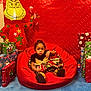 toddler, child, bean_bag, red, christmas, holiday, presents, wrapped_gifts, inflatable_grinch, candy_cane, festive_dress, blue_carpet, indoor, smiling_face, decorations, background, celebration, christmas_theme, red_backdrop, happy